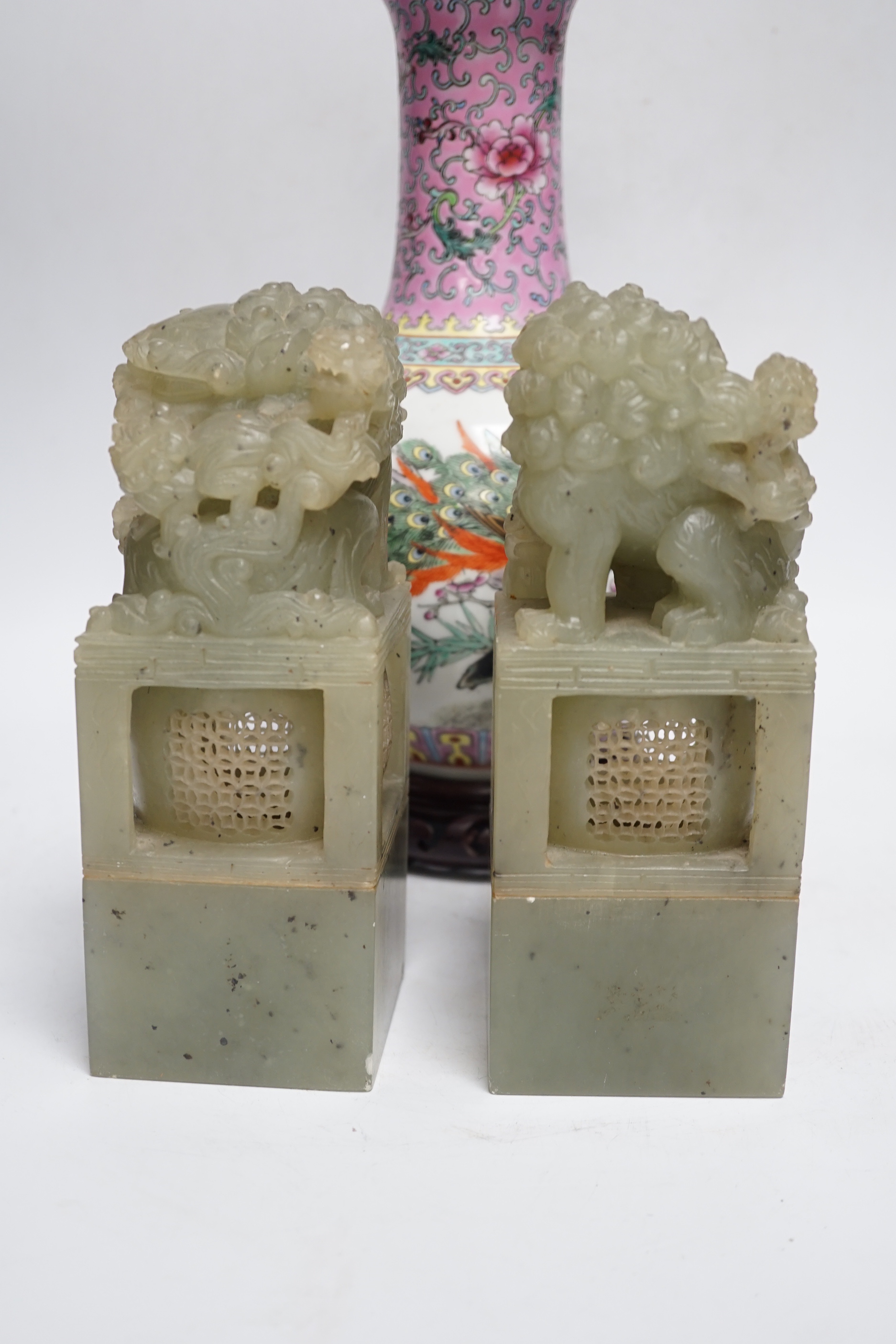 A pair of large Chinese soapstone ‘Temple Guardian lion’ seals, 21cm, and a Chinese famille rose vase, 27cm, on carved wood stand